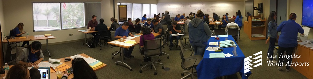 People standing/sitting getting instruction on what to do or go, the people are in a large conference room.