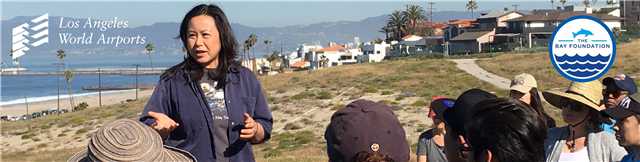 Volunteers of The Bay Foundation on top of the LAX Dunes, they are standing around a lady who is giving an announcement before they set out to pick up trash. 