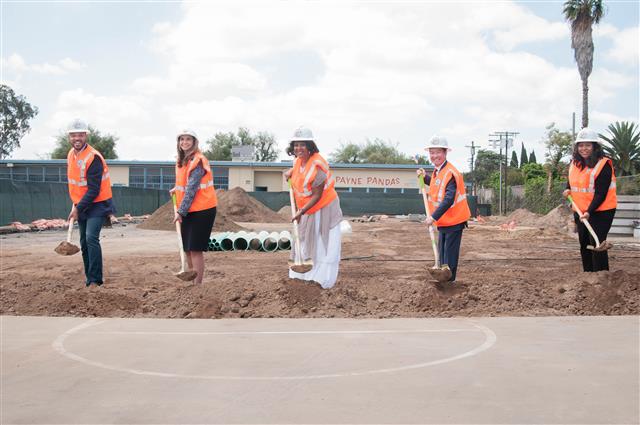 Five people wearing orange vest and holding shovel